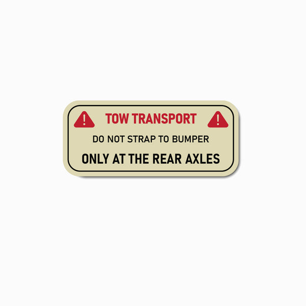 Rectangular warning label with text about tow transport and axles on a beige background